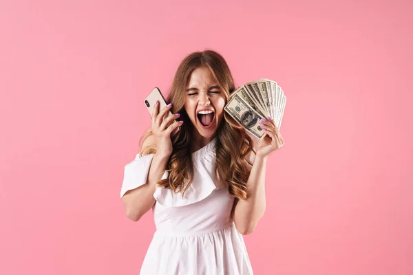 Überrascht schreiende junge hübsche Frau posiert isoliert über rosa Wand Hintergrund mit Handy hält Geld. — Stockfoto