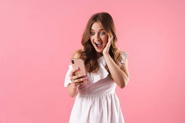 Возбужденная молодая красивая женщина позирует изолированные на розовом фоне стены с помощью мобильного телефона чата . — стоковое фото