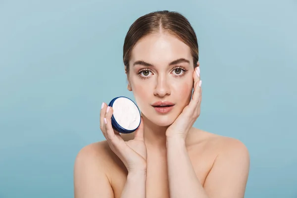 Incredibile giovane donna posa isolato su sfondo blu muro prendersi cura della sua pelle con crema . — Foto Stock