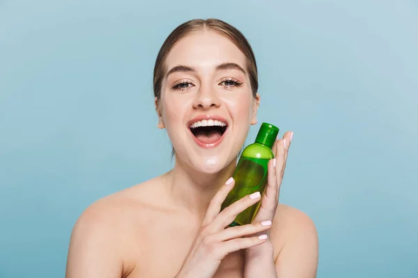 Woman posing isolated over blue wall background take care of her skin with toner.