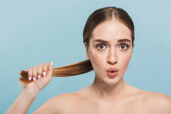 Chocado animado jovem mulher posando isolado sobre azul parede fundo tocando cabelo . — Fotografia de Stock