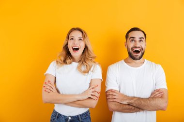 Heyecanlı genç çift erkek ve kadın portre temel t-shirt merak ve kolları geçti ile yukarı bakıyor