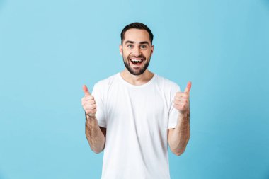 Heyecanlı genç mutlu sakallı adam jest başparmak gösteren mavi duvar arka plan üzerinde izole poz.