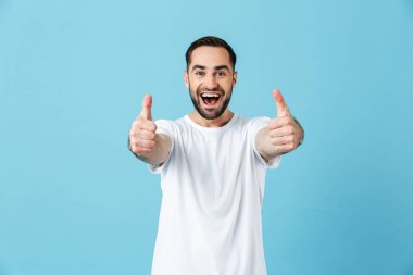 Heyecanlı genç mutlu sakallı adam mavi duvar arka plan üzerinde izole poz jest başparmak gösteren. Yaz konsepti.