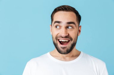 Heyecanlı genç rüya sakallı adam mavi duvar arka plan üzerinde izole poz kenara bakarak.