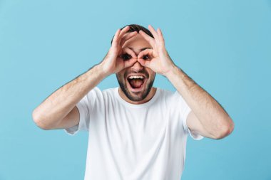 Heyecanlı genç komik mutlu sakallı adam mavi duvar arka plan üzerinde izole poz elleri ile gözlük jest gösteren eğlenmek.