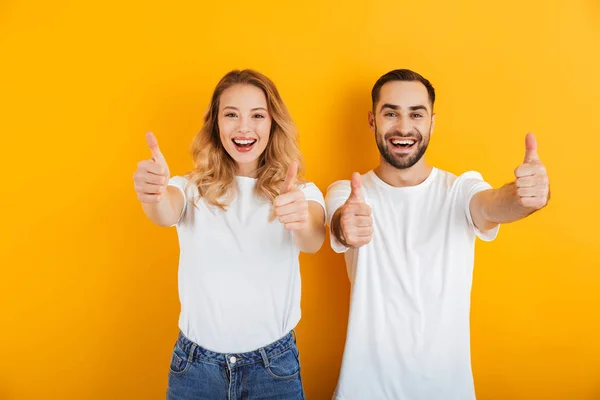 Retrato de alegre pareja joven hombre y mujer en camisetas básicas sonriendo y mostrando los pulgares hacia arriba en la cámara —  Fotos de Stock