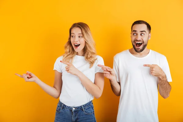 Портрет привлекательной молодой пары мужчины и женщины в основных футболках, улыбающихся и указывающих пальцами в сторону от копирайта — стоковое фото