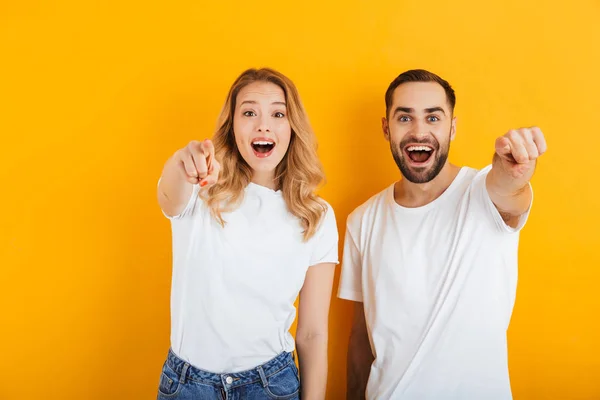 Портрет счастливой молодой пары мужчины и женщины в основных футболках, улыбающихся и указывающих пальцем на камеру — стоковое фото