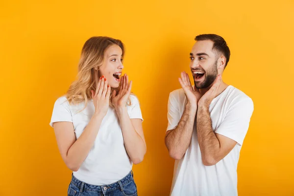 Portrét optimistického užaslého mladého páru muže a ženy v základních tričkách s úsměvem a dívali se na sebe se zbraněmi zdviženýma — Stock fotografie