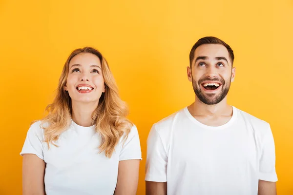Bild av bedårande par man och kvinna i grundläggande t-shirts leende medan du tittar uppåt tillsammans — Stockfoto