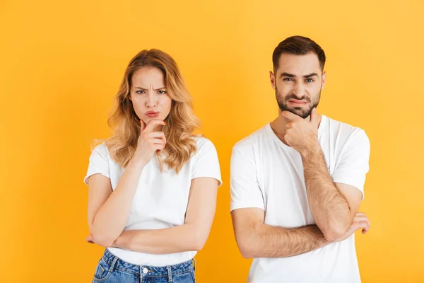 Image de couple irrité homme et femme fronçant les sourcils et touchant leurs mentons tout en regardant la caméra — Photo