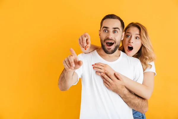 Imagen de la impactada pareja hombre y mujer expresando asombro mientras señalan los dedos a un lado en el copyspace — Foto de Stock