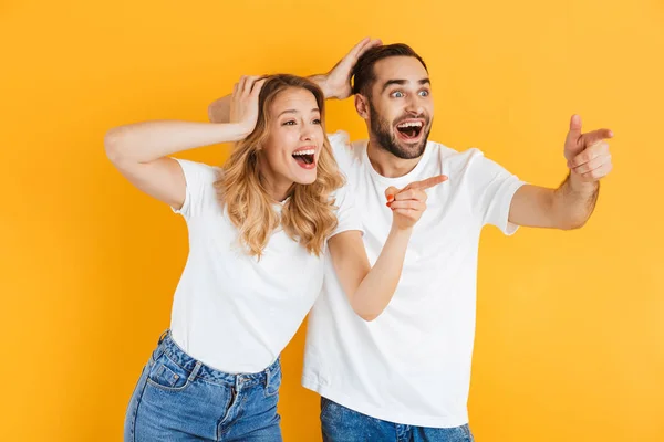 Imagem de casal animado homem e mulher expressando maravilha ao apontar os dedos de lado no copyspace — Fotografia de Stock