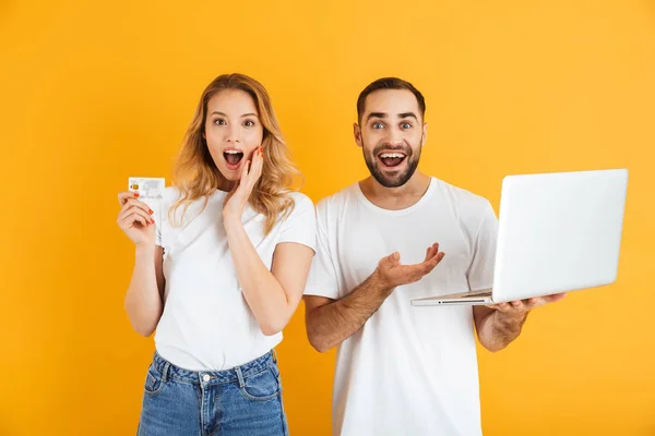 Imagen de pareja impresionada hombre y mujer expresando sorpresa mientras sostienen el ordenador portátil y la tarjeta de crédito —  Fotos de Stock