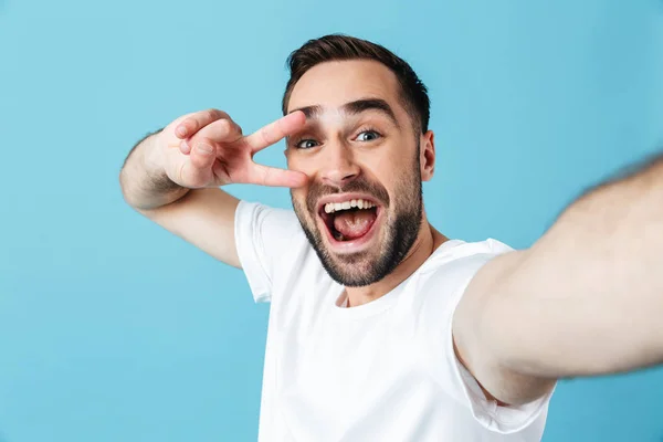 Joven alegre hombre barbudo feliz posando aislado sobre fondo de pared azul tomar una selfie por la cámara . —  Fotos de Stock