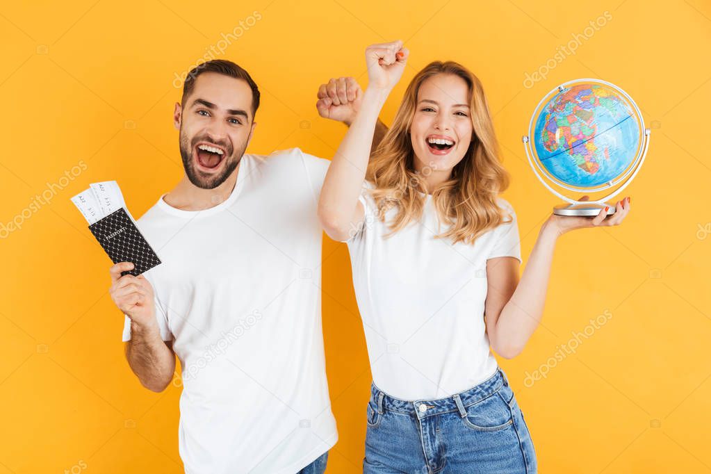 Image of cheerful couple rejoicing while holding earth globe and passport with travel tickets