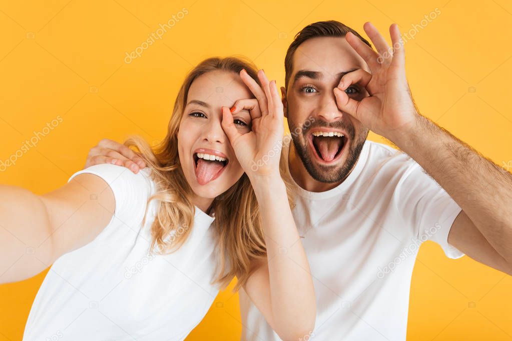 Image of joyful couple rejoicing and sticking out tongues while showing ok sign together