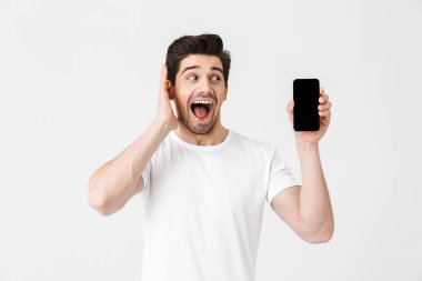 Heyecanlı mutlu genç adam cep telefonu ekran gösteren beyaz duvar arka plan üzerinde izole poz.