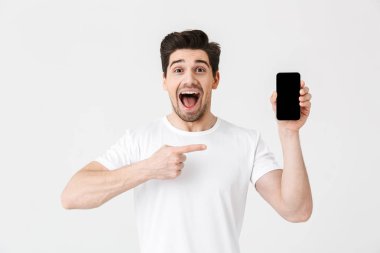 Heyecanlı mutlu genç adam cep telefonu ekran gösteren beyaz duvar arka plan üzerinde izole poz.