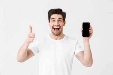 Heyecanlı mutlu genç adam cep telefonu ekran gösteren beyaz duvar arka plan üzerinde izole poz.