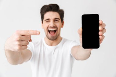 Heyecanlı mutlu genç adam cep telefonu ekran gösteren beyaz duvar arka plan üzerinde izole poz.