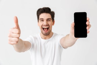 Heyecanlı mutlu genç adam cep telefonu ekran gösteren beyaz duvar arka plan üzerinde izole poz.