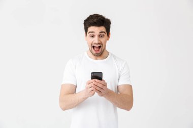 Heyecanlı mutlu genç adam cep telefonu kullanarak beyaz duvar arka plan üzerinde izole poz.
