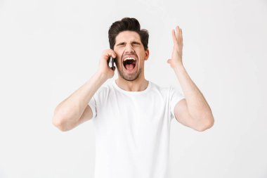 Mutlu heyecanlı şok genç adam cep telefonu ile konuşurken beyaz duvar arka plan üzerinde izole poz.