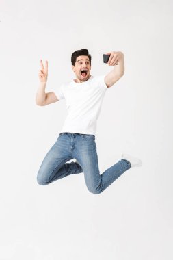 Cep telefonu kullanarak beyaz duvar arka plan üzerinde izole poz genç adam selfie çekmek.