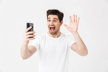 Cep telefonu kullanarak beyaz duvar arka plan üzerinde izole poz genç adam selfie çekmek.