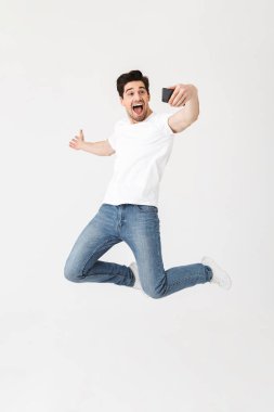 Cep telefonu kullanarak beyaz duvar arka plan üzerinde izole poz genç adam selfie çekmek.