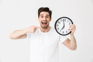 Şok heyecanlı mutlu genç adam saat tutan beyaz duvar arka plan üzerinde izole poz.