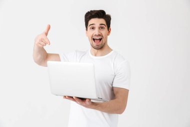 Mutlu heyecanlı genç adam dizüstü bilgisayar işaret kullanarak beyaz duvar üzerinde izole poz.