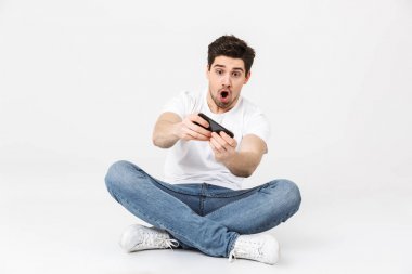 Gergin genç adam cep telefonu ile beyaz duvar arka plan üzerinde izole poz oyunları.