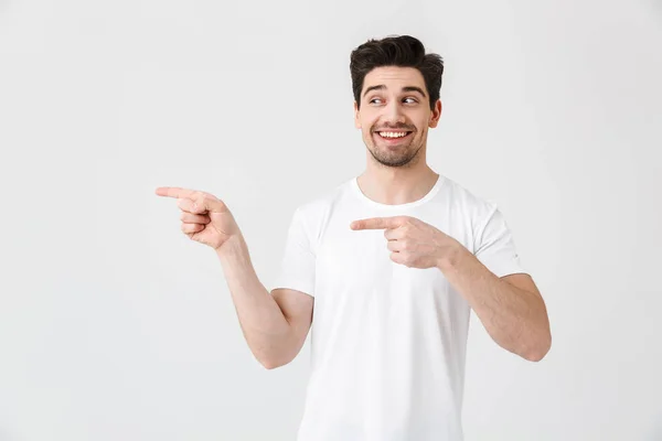 Emocionado joven posando aislado sobre fondo blanco de la pared apuntando . — Foto de Stock