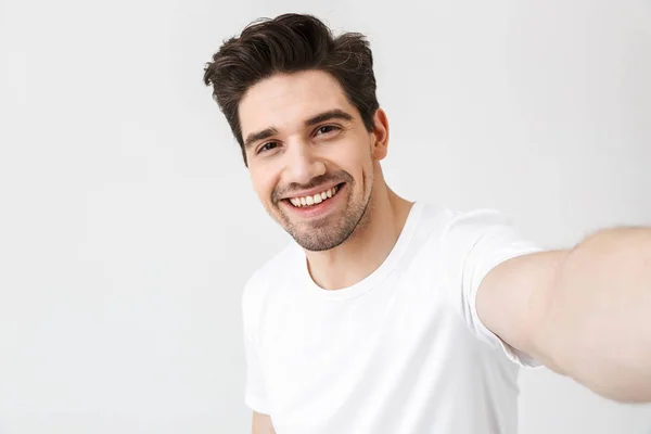 Aufgeregter glücklicher junger Mann posiert isoliert über weißem Wandhintergrund und macht ein Selfie mit der Kamera. — Stockfoto