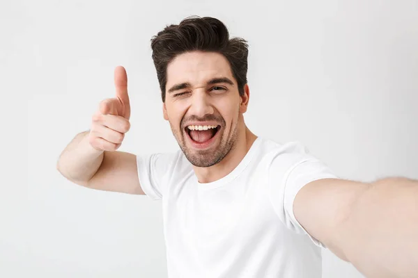 Aufgeregter glücklicher junger Mann posiert isoliert über weißem Wandhintergrund und macht ein Selfie mit der Kamera. — Stockfoto