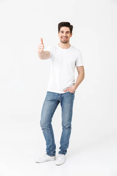 Возбужденный молодой человек позирует изолированно на фоне белой стены, показывая большой палец вверх жестом . — стоковое фото