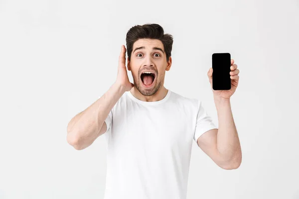 Emocionado joven feliz posando aislado sobre fondo de pared blanca que muestra la pantalla del teléfono móvil . — Foto de Stock