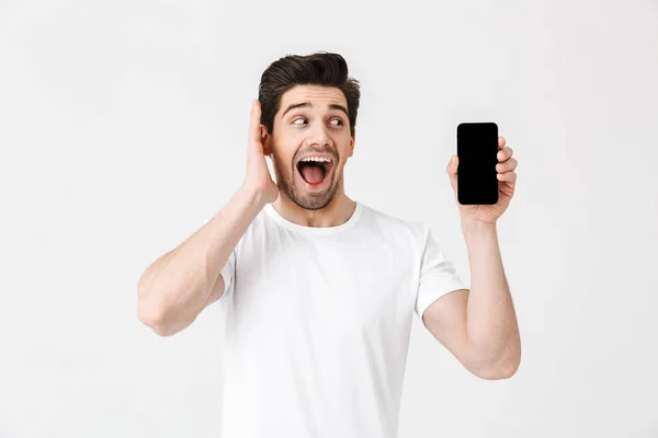 Jovem feliz excitado posando isolado sobre fundo da parede branca mostrando exibição de telefone celular . — Fotografia de Stock