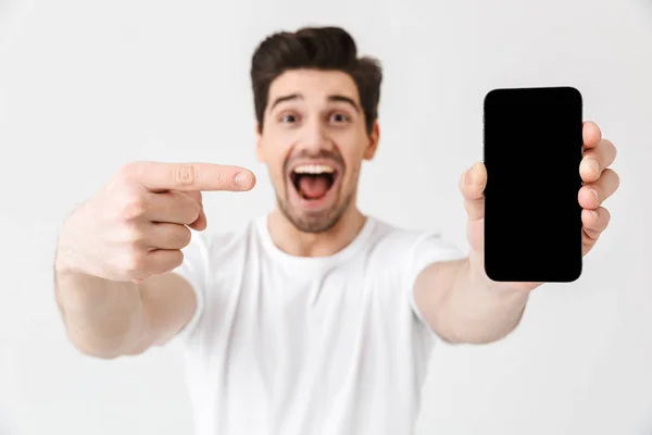 Emocionado joven feliz posando aislado sobre fondo de pared blanca que muestra la pantalla del teléfono móvil . — Foto de Stock