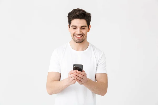 Opgewonden gelukkig jonge man poseren geïsoleerd over witte muur achtergrond met behulp van mobiele telefoon. — Stockfoto