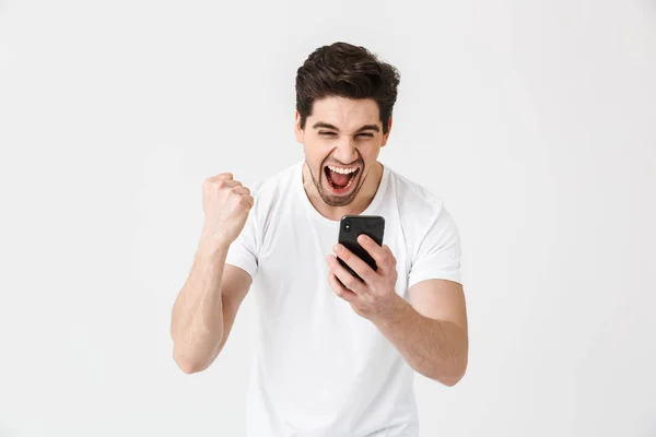 Emocionado joven feliz posando aislado sobre fondo blanco de la pared usando el teléfono móvil . — Foto de Stock