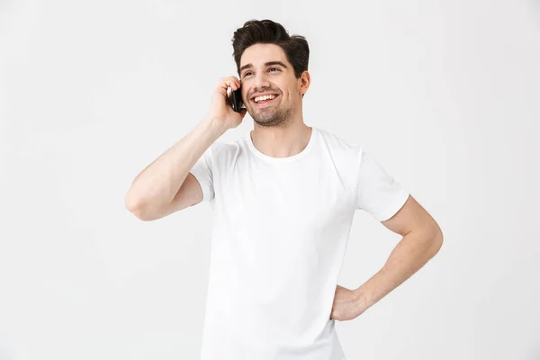 Felice giovane uomo posa isolato su sfondo bianco muro parlando dal telefono cellulare . — Foto Stock