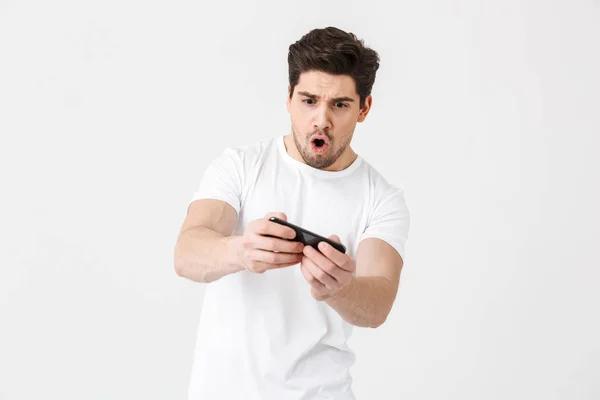 Opgewonden nerveuze emotionele jonge man poseren geïsoleerd over witte muur achtergrond spelen games door mobiele telefoon. — Stockfoto