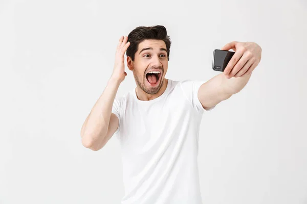 Feliz joven emocional posando aislado sobre fondo blanco de la pared tomar selfie por teléfono móvil . — Foto de Stock