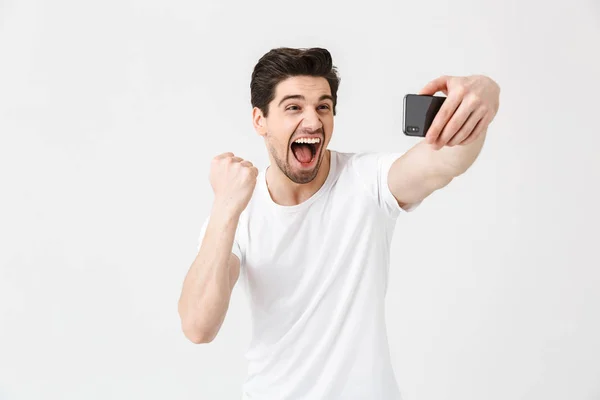 Feliz joven emocional posando aislado sobre fondo blanco de la pared tomar selfie por teléfono móvil . — Foto de Stock