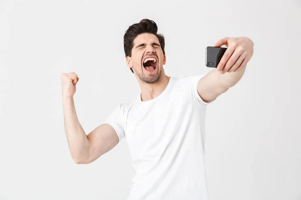 Feliz joven emocional posando aislado sobre fondo blanco de la pared tomar selfie por teléfono móvil . — Foto de Stock