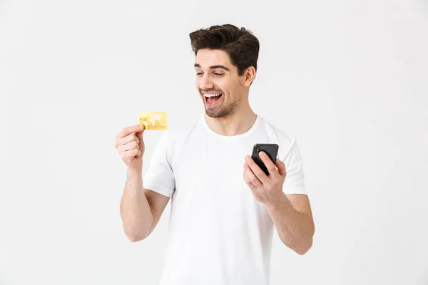 兴奋的快乐年轻人假扮隔离在白墙背景用手机拿着信用卡. — 图库照片